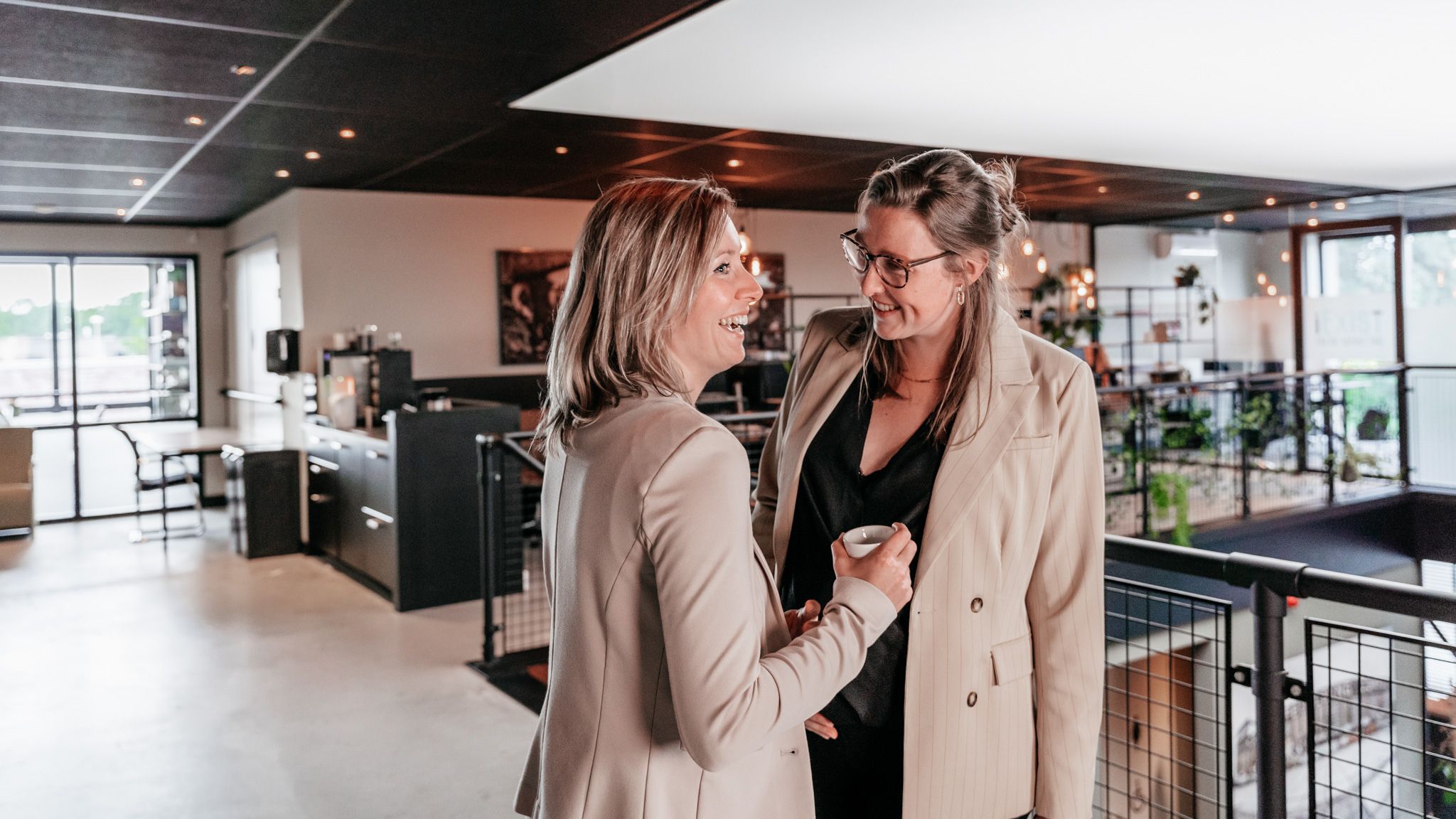 Twee collega's lachen met elkaar in een moderne kantoorruimte