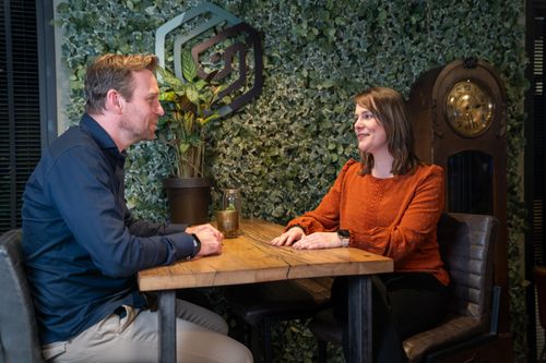 Twee collega's in gesprek aan een vergadertafel in een moderne kantoorruimte