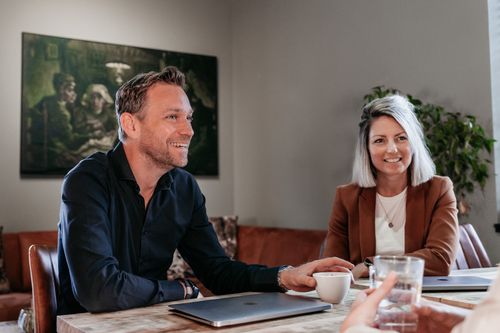 Drie collega's van Rochewood in gesprek aan een vergadertafel met een glas water en een kop koffie in de voorgrond