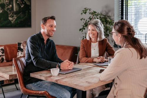 Drie collega's van Rochewood in gesprek aan een vergadertafel met een glas water en een kop koffie in de voorgrond