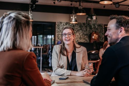 Drie collega's van Rochewood in gesprek aan een vergadertafel met een glas water in de voorgrond