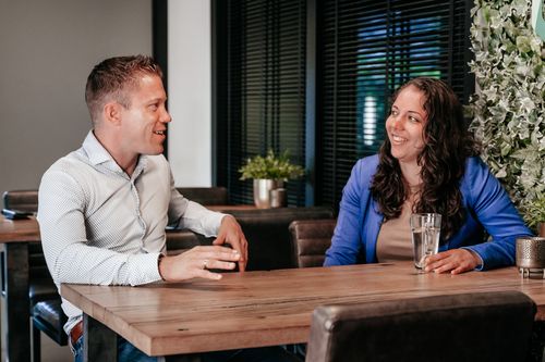Twee collega's van Rochewood in gesprek aan een vergadertafel met een glas water in de voorgrond