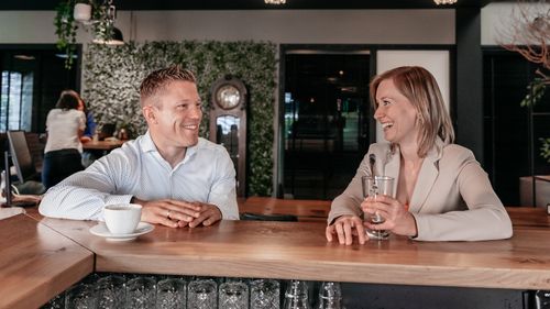Twee collega's in gesprek aan de bar in het kantoor van Rochewood, met een glas water en koffiekop op de voorgrond