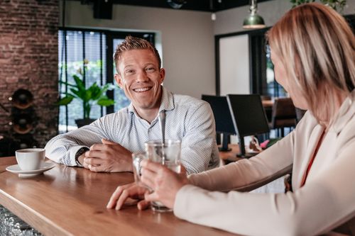 Twee collega's in gesprek aan de bar in het kantoor van Rochewood, met een glas water en koffiekop op de voorgrond