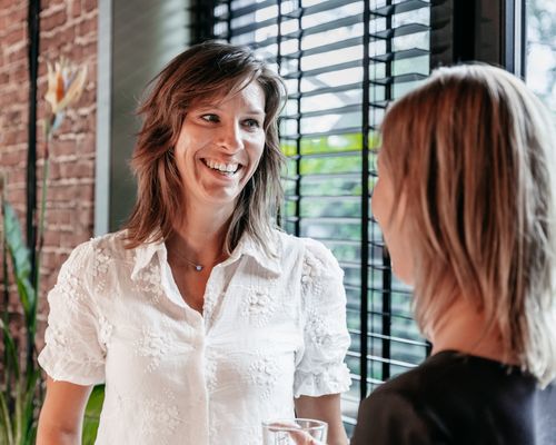 Twee collega's van Rochewood praten en lachen met elkaar bij een deur in een kantooromgeving