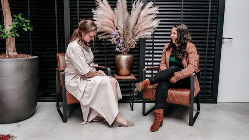 Twee collega's van Rochewood lachen met elkaar zittend in stoelen in een moderne werkomgeving