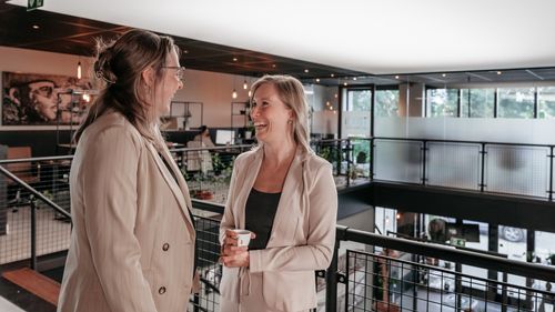 Twee collega's lachen met elkaar in een moderne kantoorruimte