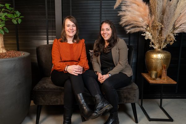 Twee collega's van Rochewood zitten op een bankje in een moderne kantooromgeving in gesprek en lachen met elkaar