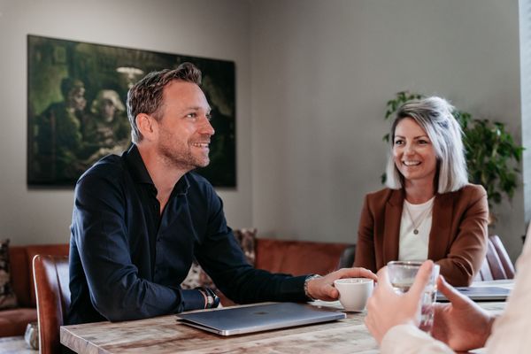 Drie collega's van Rochewood in gesprek aan een vergadertafel met een glas water en een kop koffie in de voorgrond