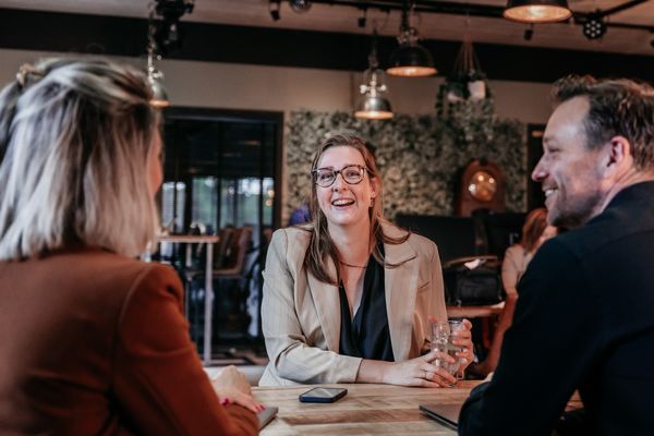 Drie collega's van Rochewood in gesprek aan een vergadertafel met een glas water in de voorgrond