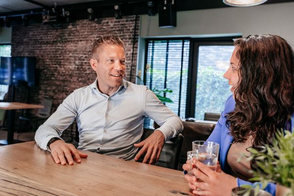 Twee collega's van Rochewood in gesprek aan een vergadertafel met een glas water in de voorgrond