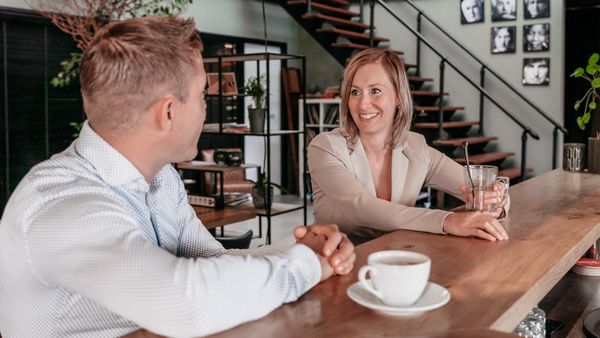 Twee collega's in gesprek aan de bar in het kantoor van Rochewood, met een glas water en koffiekop op de voorgrond
