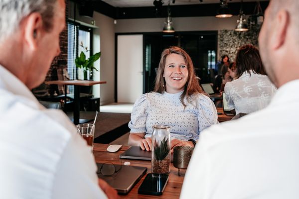 Drie collega’s van Rochewood in gesprek aan een vergadertafel, op de achtergrond zie je de lunchruimte van het kantoor