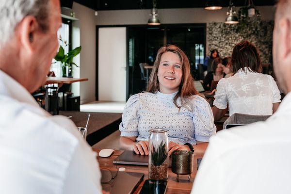 Drie collega’s van Rochewood in gesprek aan een vergadertafel, op de achtergrond zie je de lunchruimte van het kantoor