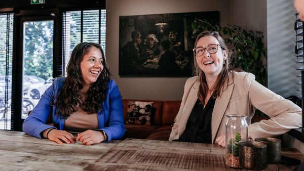 Twee collega's van Rochewood in gesprek en lachen met elkaar aan een vergadertafel