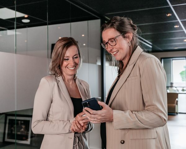 Twee collega’s van Rochewood bekijken samen iets op een telefoon en lachen, in een moderne kantoorruimte