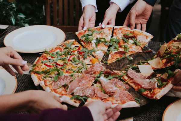 Een tafel met een grote pizza waar meerdere mensen een stuk van pakken