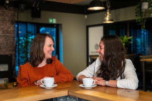 Twee collega's in gesprek aan de bar in het kantoor van Rochewood, met twee koffiekopjes op de voorgrond
