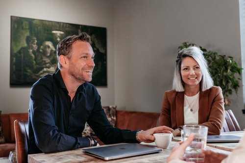 Drie collega's van Rochewood in gesprek aan een vergadertafel met een glas water en een kop koffie in de voorgrond