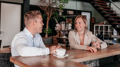Twee collega's in gesprek aan de bar in het kantoor van Rochewood, met een glas water en koffiekop op de voorgrond