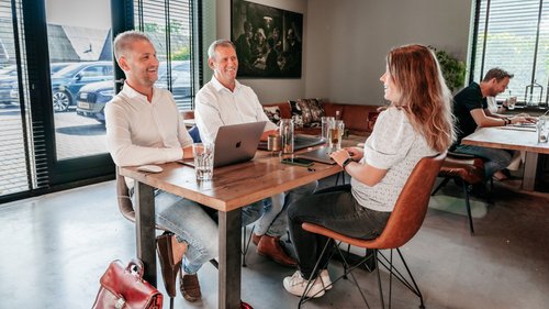 Drie collega’s van Rochewood in gesprek aan een vergadertafel, op de achtergrond zie je de lunchruimte van het kantoor