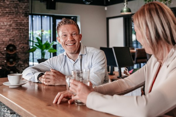 Twee collega's in gesprek aan de bar in het kantoor van Rochewood, met een glas water en koffiekop op de voorgrond