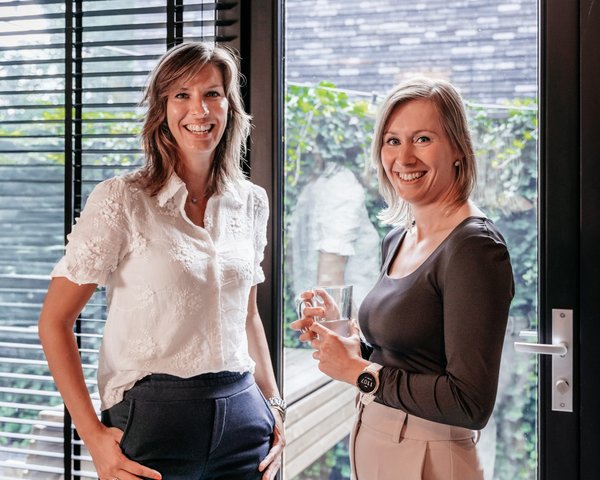 Twee collega's van Rochewood praten en lachen met elkaar bij een deur in een kantooromgeving