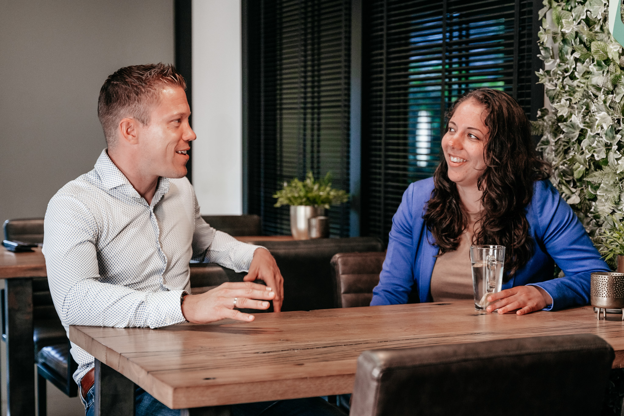 Twee collega's van Rochewood in gesprek aan een vergadertafel met een glas water in de voorgrond